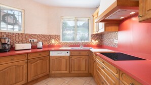 A kitchen with wooden cabinets, a red countertop, a dishwasher, and a window with a wreath. - Zen House in the Pyrenees, Private Terrace and Wi-Fi (Coarraze)