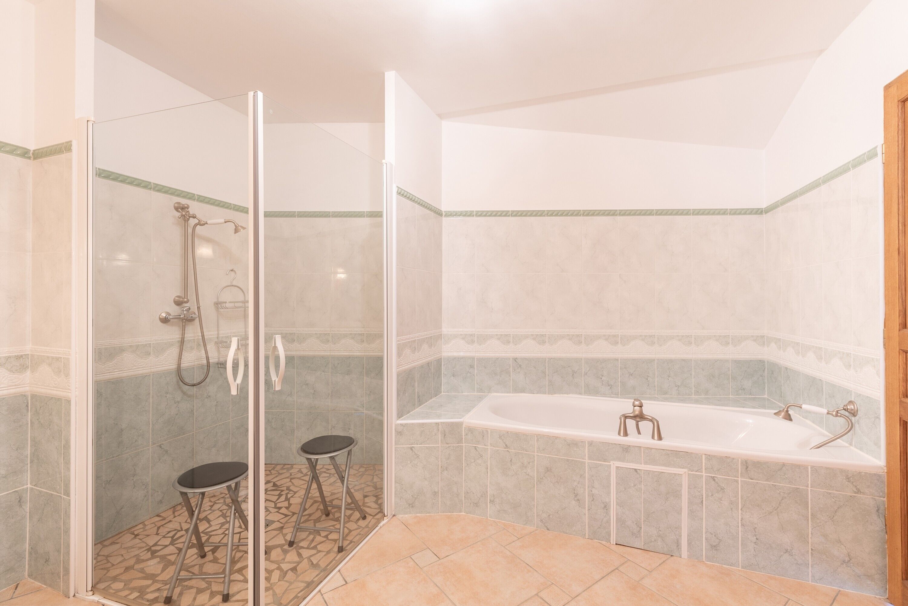 A bathroom with a glass-enclosed shower, a bathtub, and a small stool.