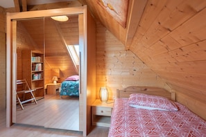 Een houten kamer met een bed, een nachtkastje, een lamp, een boekenplank en een ladder.