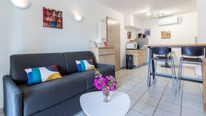 Un soggiorno moderno con un divano, un tavolino da caffè con fiori, una zona pranzo con sedie e una cucina sullo sfondo.