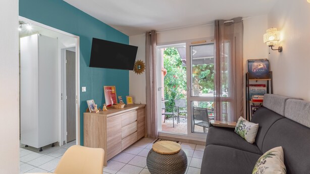 A living room with a sofa, a coffee table, a TV mounted on the wall, and a sliding glass door leading to an outdoor area. - 'Meu Descan' Apartment with Shared Pool, Private Terrace, and Air Conditioning (Cerbère)
