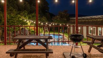 An outdoor patio with picnic tables, a barbecue grill, and a swimming pool.