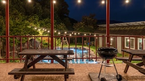 Eine Terrasse im Freien mit Picknicktischen, einem Grill und einem Swimmingpool.