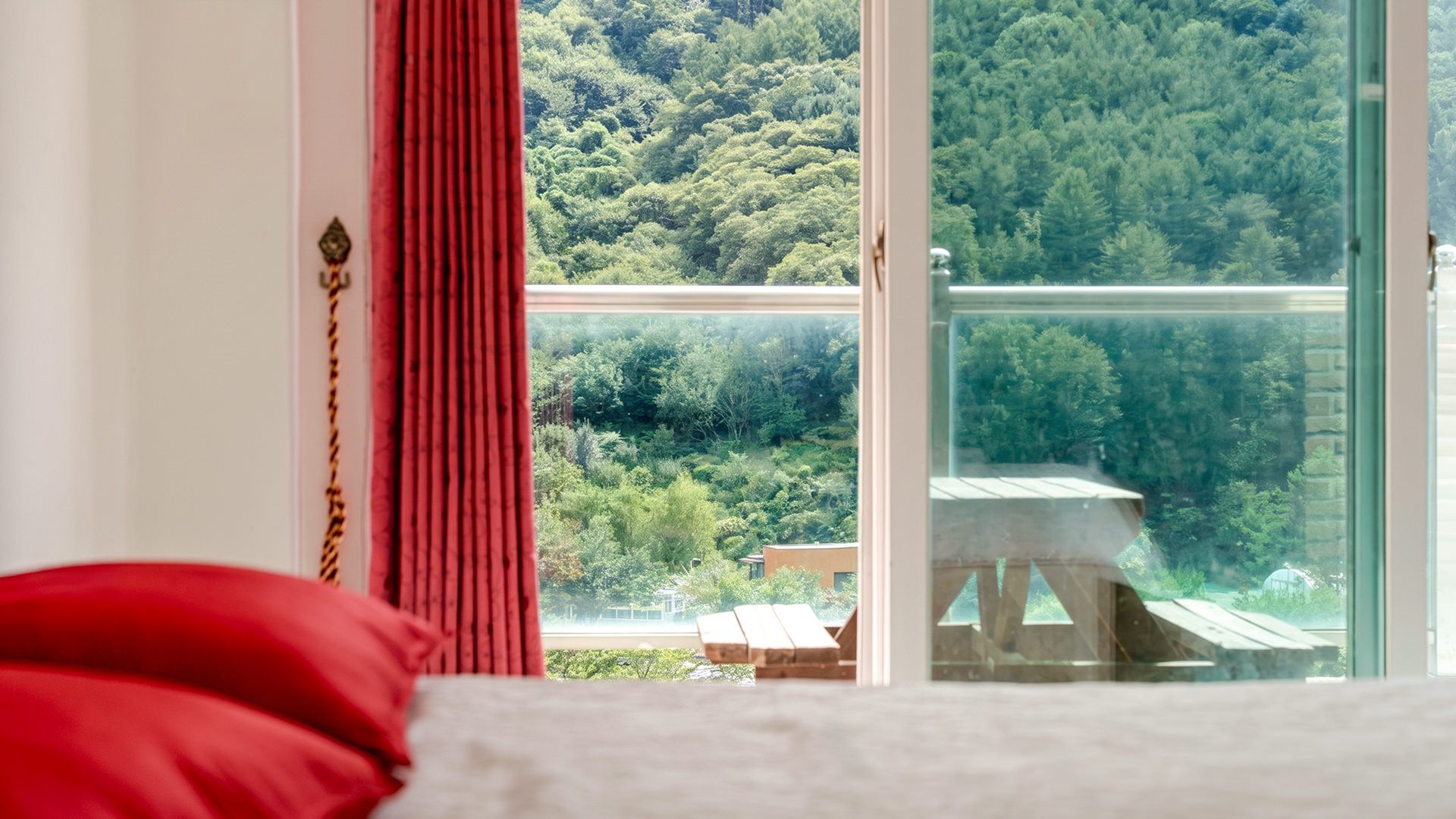 A bedroom with a large window overlooking a forested area.