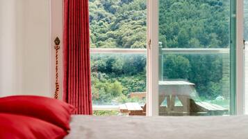 A bedroom with a large window overlooking a forested area.
