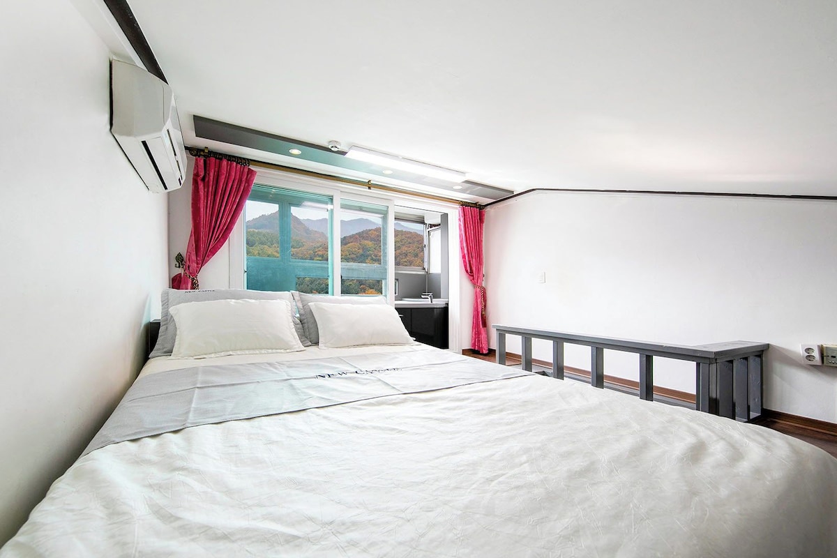 Une chambre à coucher avec un lit, une fenêtre avec des rideaux, un radiateur et une vue sur un lac et des montagnes.