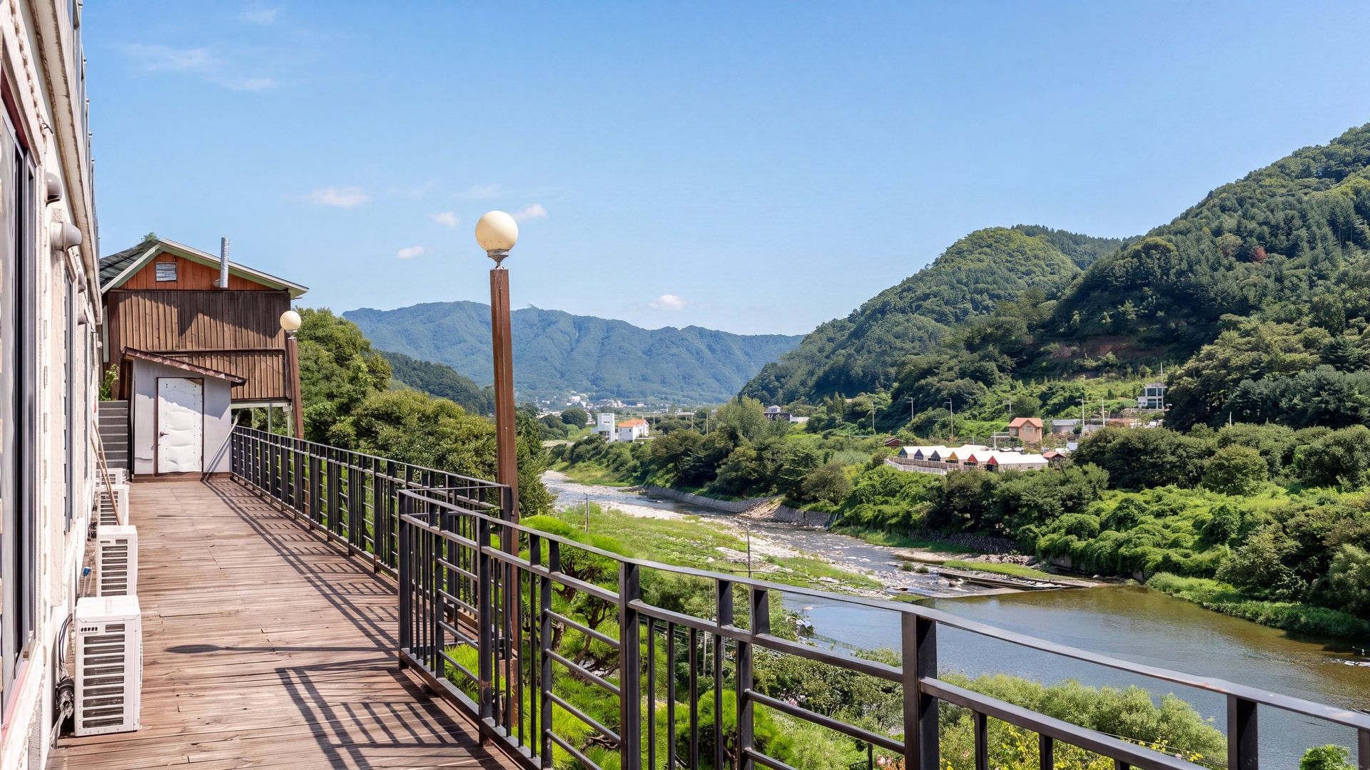 A wooden deck with a metal railing overlooking a river and mountains.