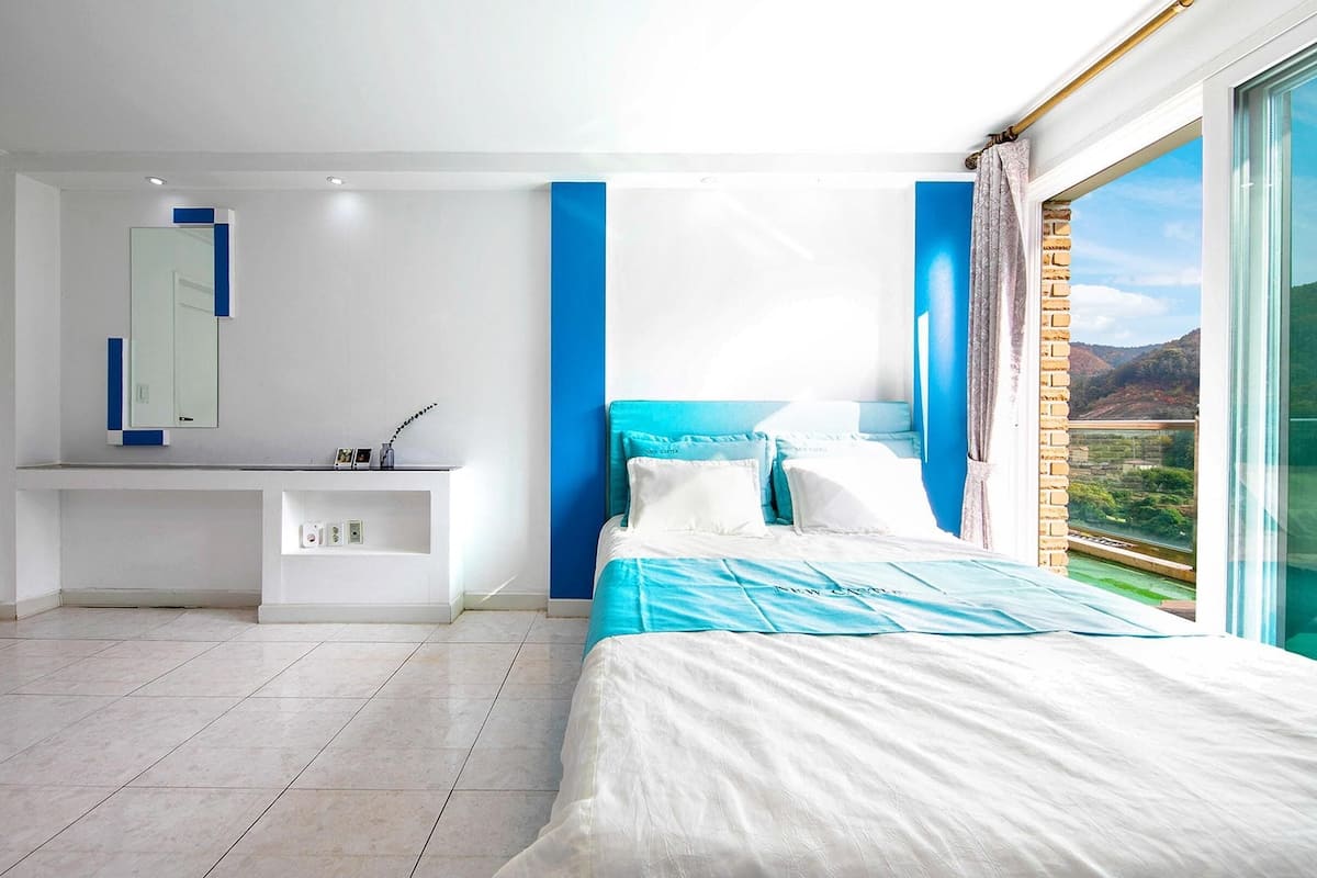 Een moderne slaapkamer met een groot bed, een inbouw bureau en een groot raam met uitzicht op de omgeving.