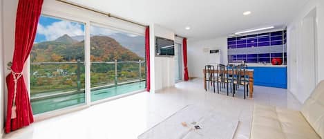 A spacious living area with a large sliding glass door leading to a balcony, a dining area with a table and chairs, and a kitchen with blue cabinets and a red appliance.