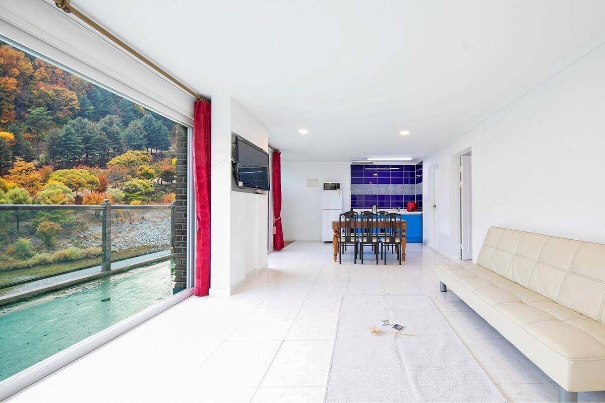 Een modern interieur met een eethoek, een bank en uitzicht op een meer met herfstbomen.