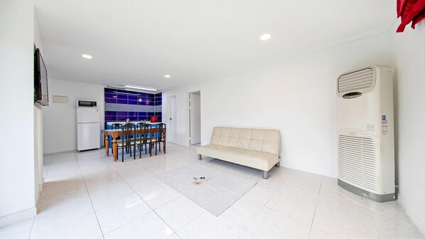 Una sala de estar moderna con un sofá color beige, un comedor con mesa y sillas, y una cocina con refrigerador y salpicadero de azulejos azules.