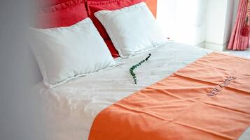 A bed with white and orange bedding, a green plant decoration, and a pillow with a red accent.