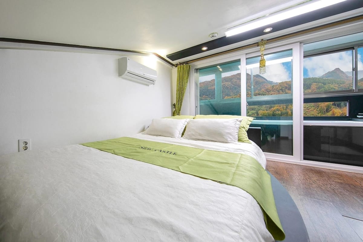 Een slaapkamer met een bed, een raam met uitzicht op een berg, en een airconditioning aan de muur.