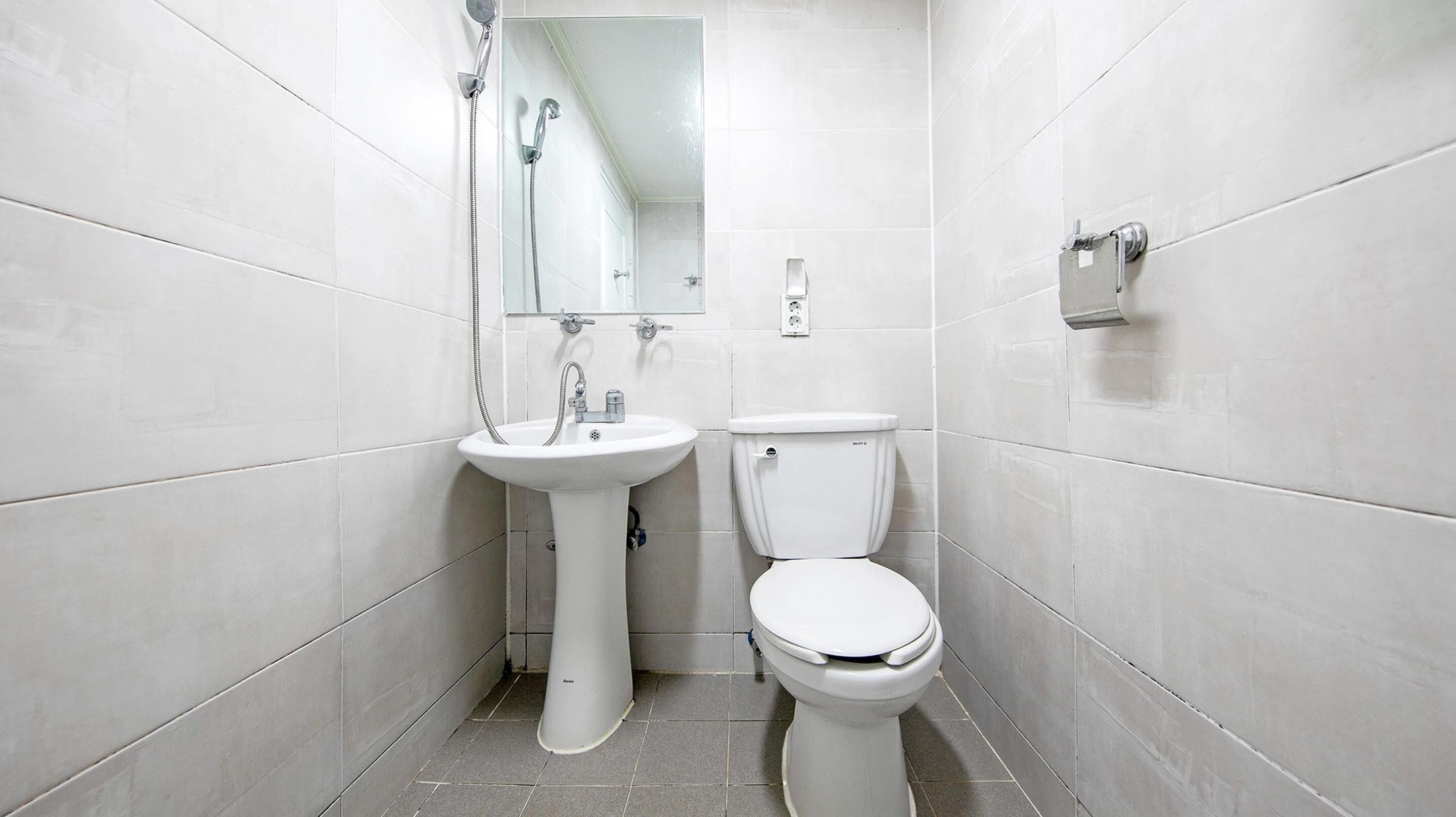 A small, white-tiled bathroom with a pedestal sink, a toilet, and a shower.