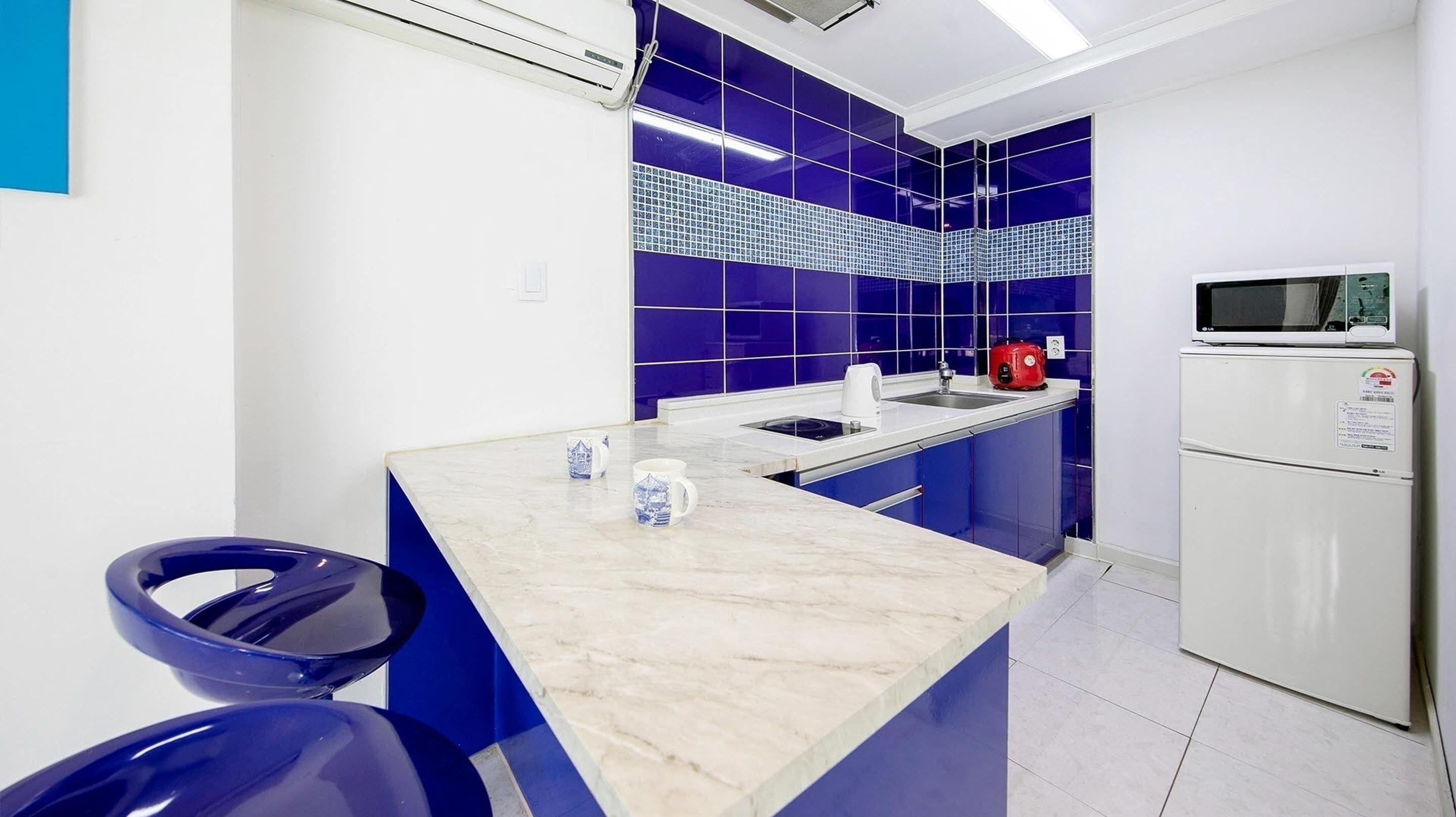 A modern kitchen with a marble countertop, blue cabinets, a microwave, and a refrigerator.
