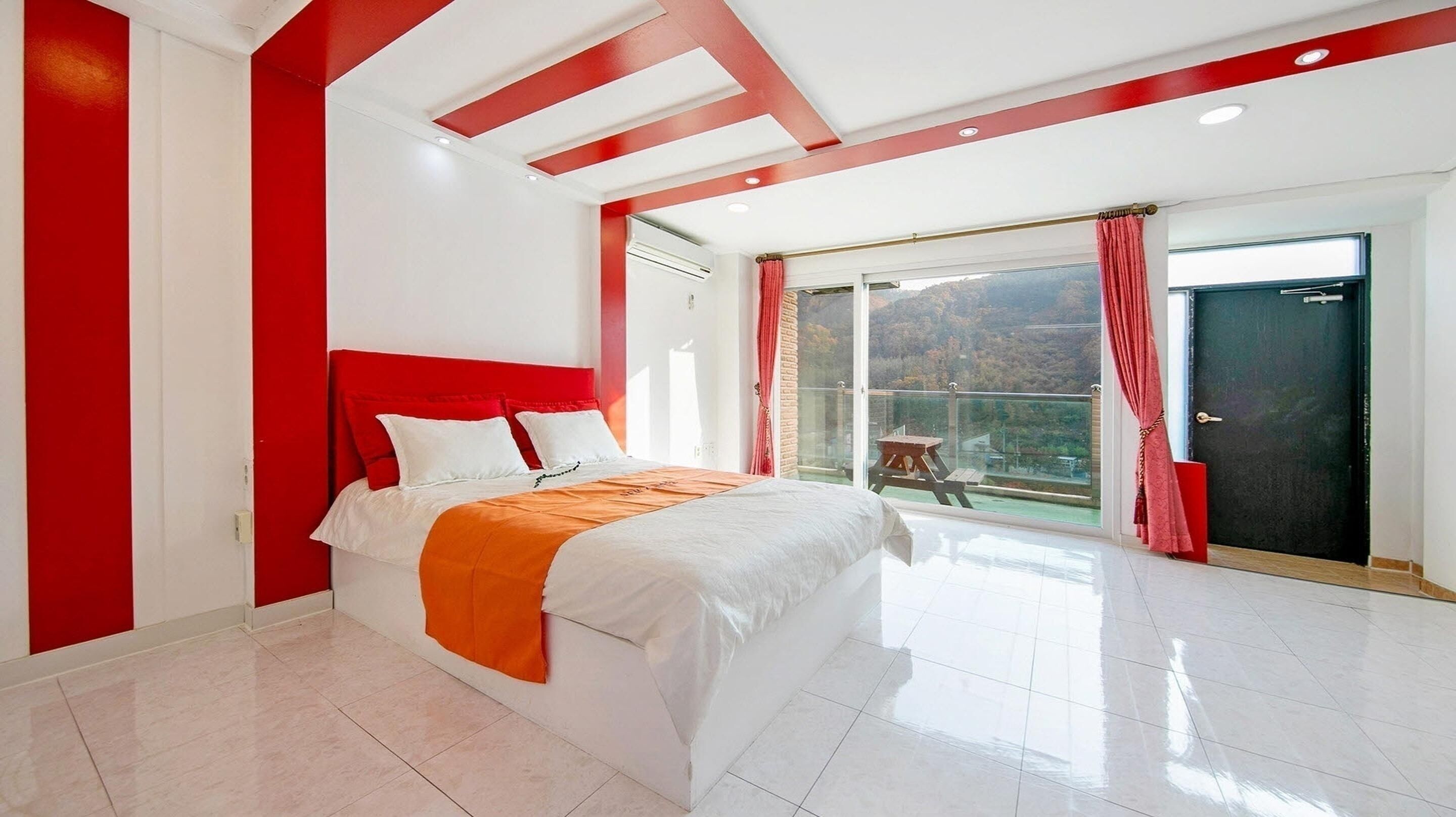 Un dormitorio moderno con una cama grande, un balcón con vistas y una decoración en tonos rojo y blanco.