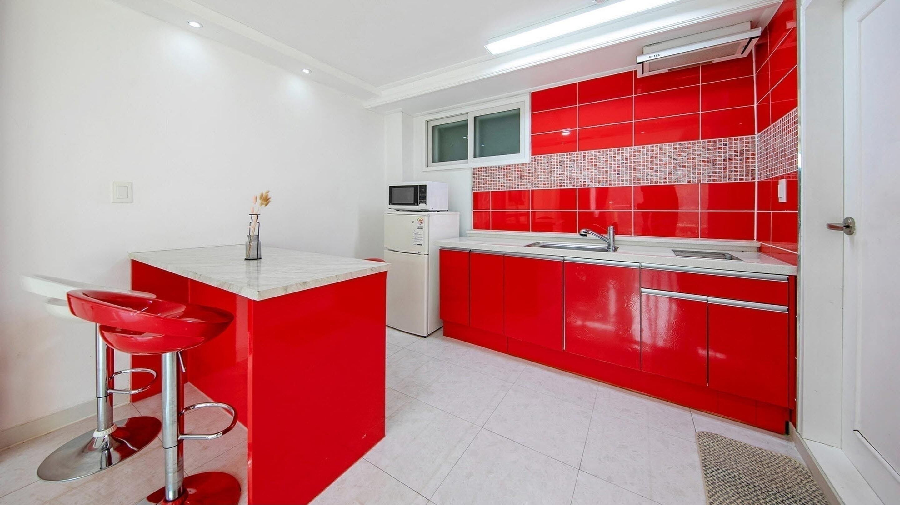 Una cucina moderna con mobili rossi, ripiani bianchi e un forno a microonde integrato.