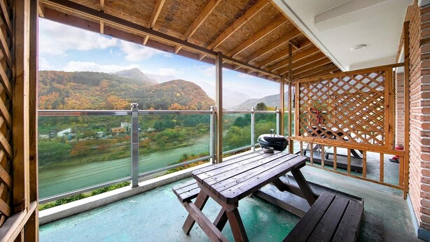 Un balcon doté d’une table et de bancs en bois, offrant une vue panoramique sur les montagnes et une rivière.