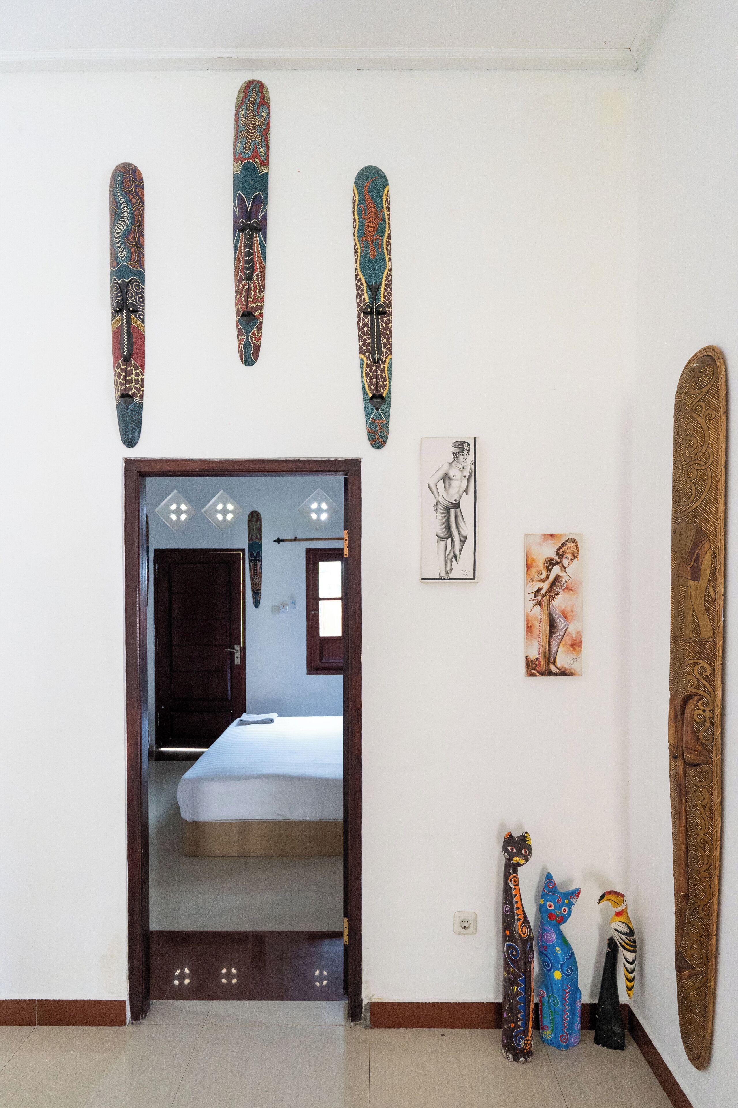 A room with a bed, a wooden door, and various decorative items including wall hangings and sculptures.