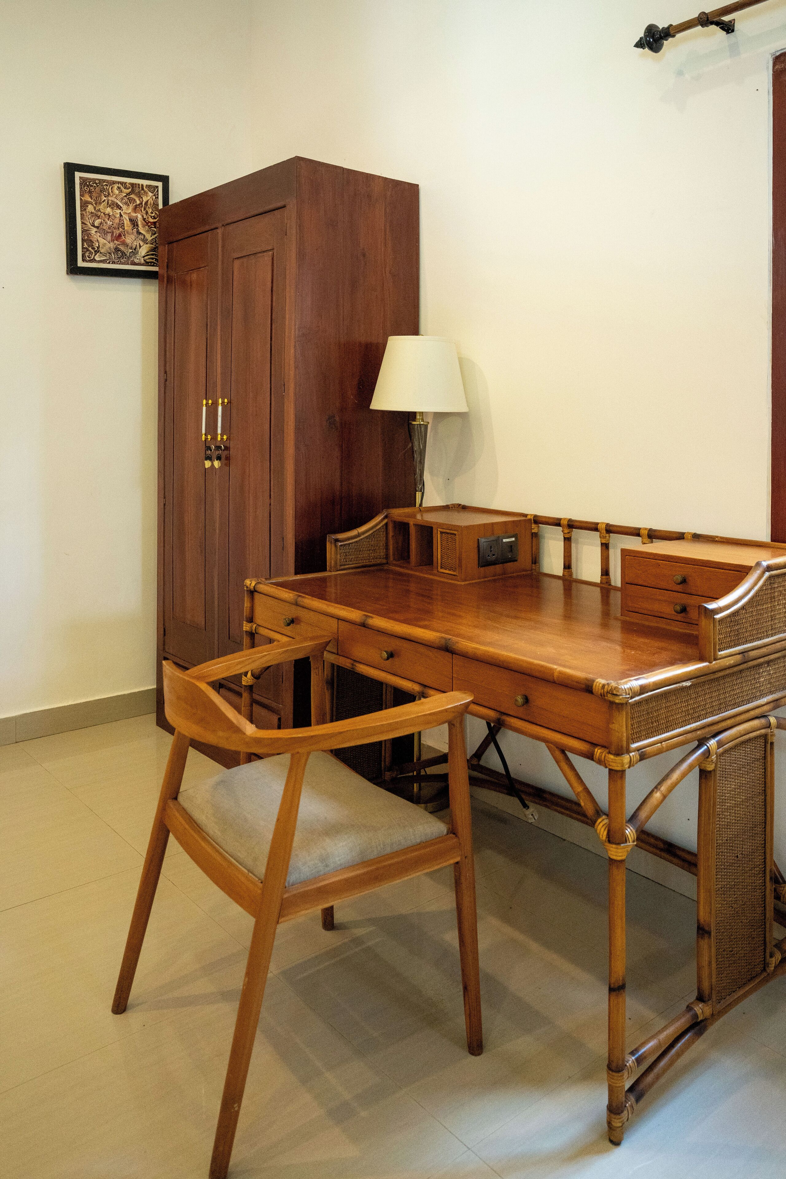 A wooden desk with a lamp, a chair, and a cabinet in a room with tiled flooring.