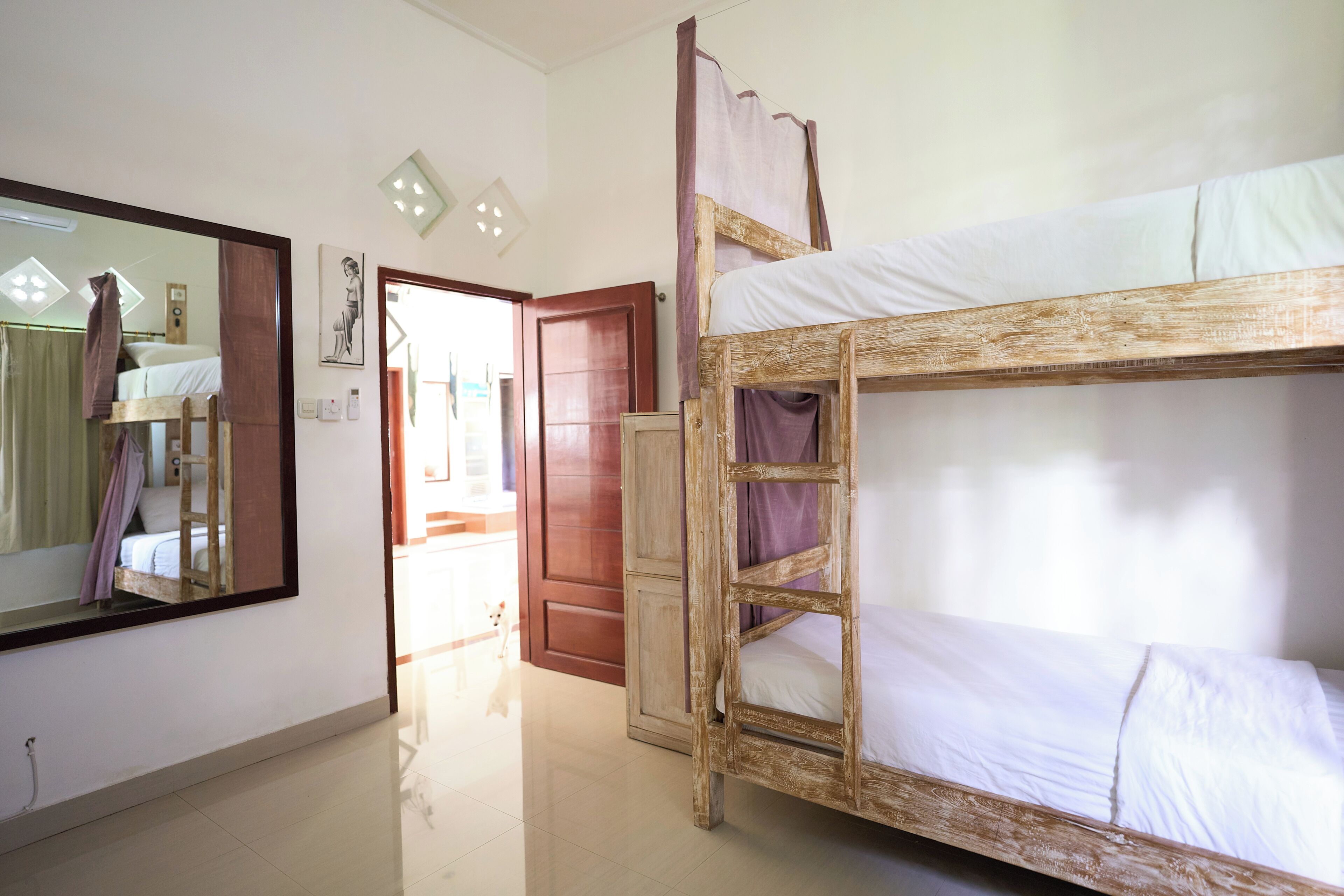 A room with a bunk bed, a wooden wardrobe, a mirror, and a door leading to another room.