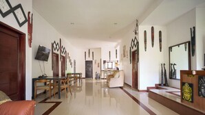 A spacious living area with a dining table and chairs, a sofa, and a reception desk with a Buddha statue. - Seva Hotel (Karangasem)