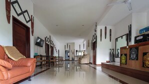 A spacious living area with a leather sofa, wooden furniture, and a reception desk with Buddha statues. - Seva Hotel (Karangasem)