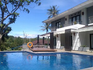 Un espace piscine moderne offrant une vue dégagée sur la piscine, avec une bouée de sauvetage et un bâtiment doté d’un balcon.