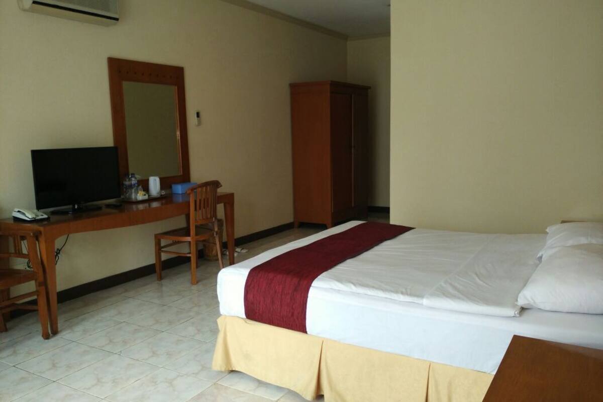 A hotel room with a bed, a desk with a chair, a television, and a wardrobe.