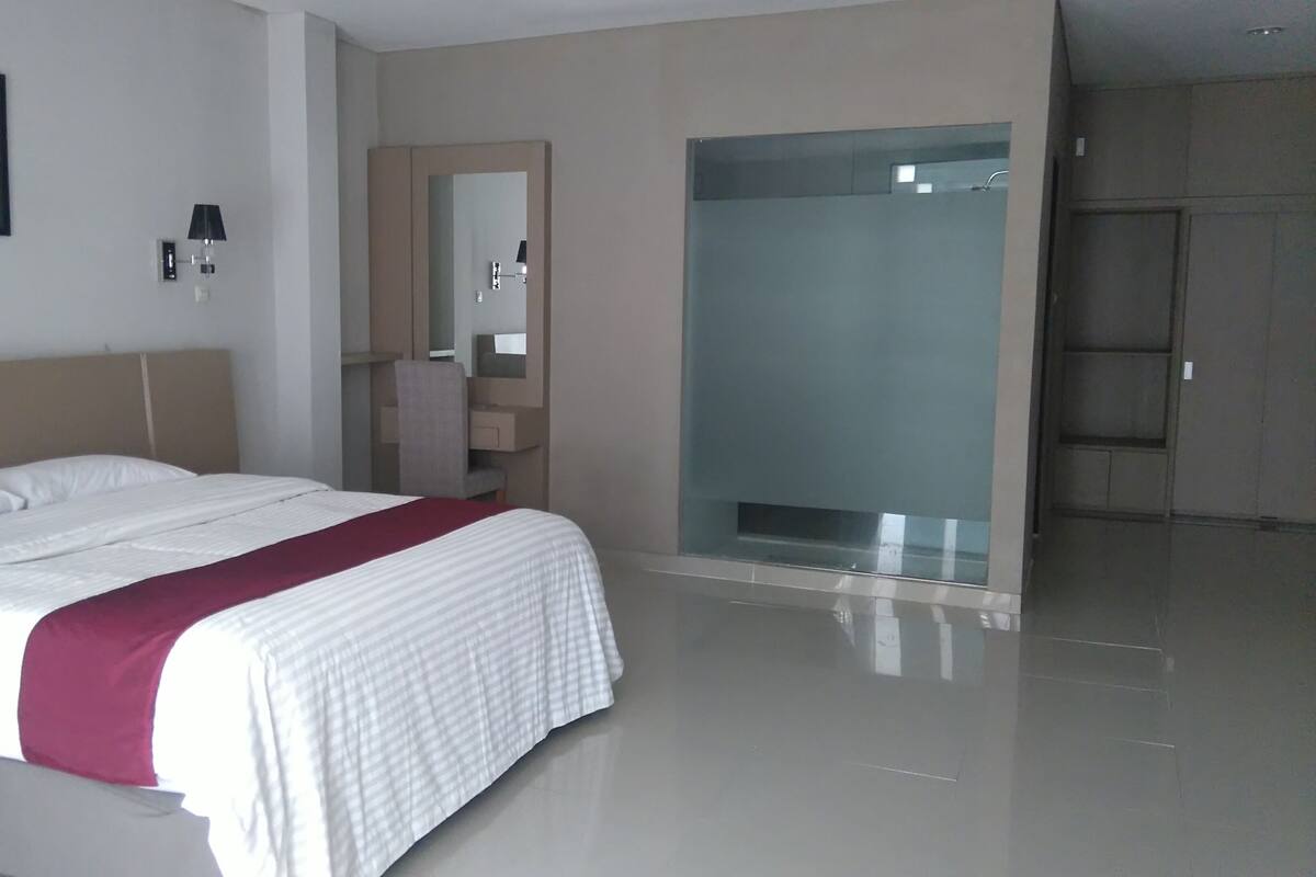 A modern hotel room with a large bed, a vanity with a mirror, and a walk-in shower.