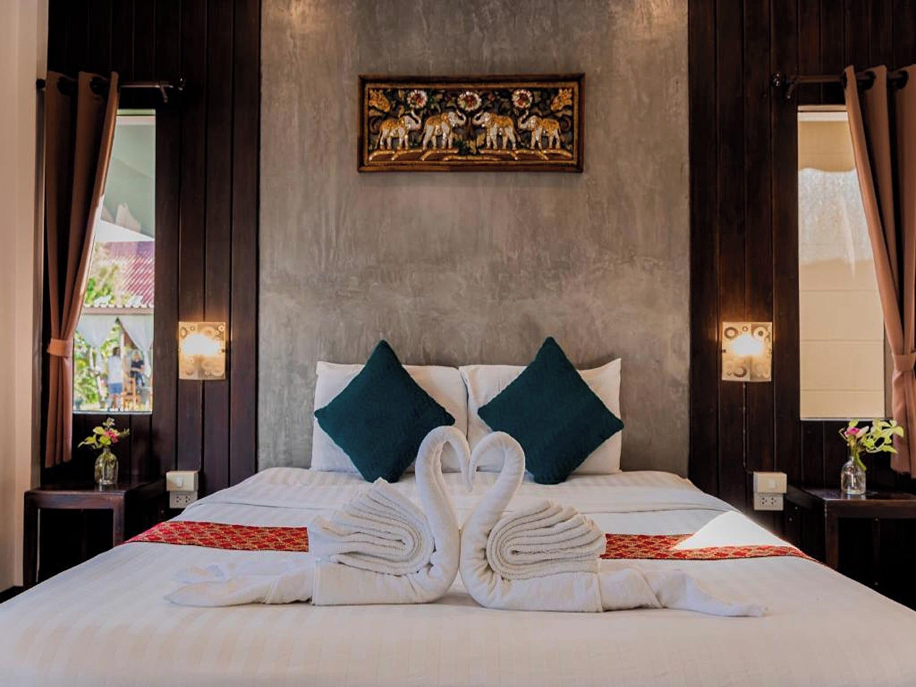 A hotel room with a bed, two pillows, a wall-mounted artwork, and a window with curtains.