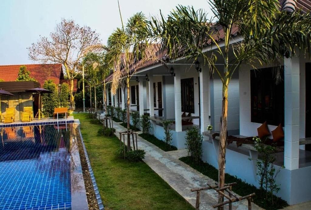 Zona junto a la piscina con piscina, un área de estar techada y una hilera de edificios blancos con ventanas y puertas.
