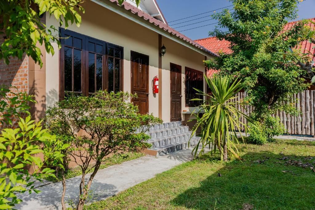 Ein Haus mit Backsteinfassade, großen Fenstern, einem roten Ziegeldach und einem kleinen Garten mit einer Palme.