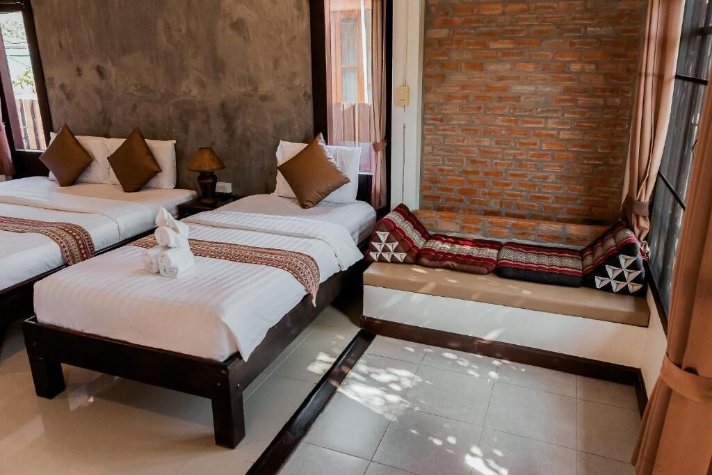 A hotel room with two beds, a bench, a brick wall, and a window with curtains.
