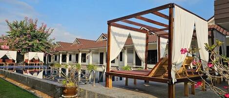 A courtyard with a wooden canopy bed, a pool, and a building with a tiled roof.