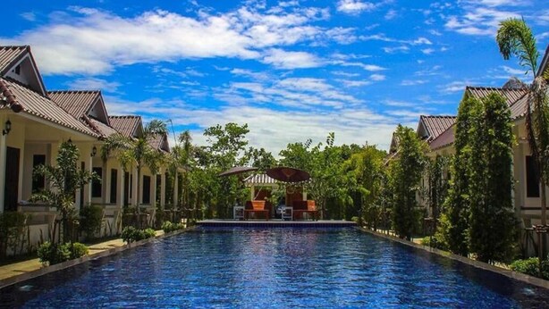 A swimming pool with a covered seating area, surrounded by buildings with tiled roofs and lush greenery.