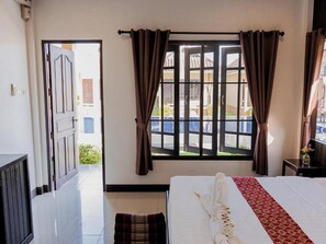 Habitación de hotel con cama, ventana con cortinas, una puerta y vistas al exterior.