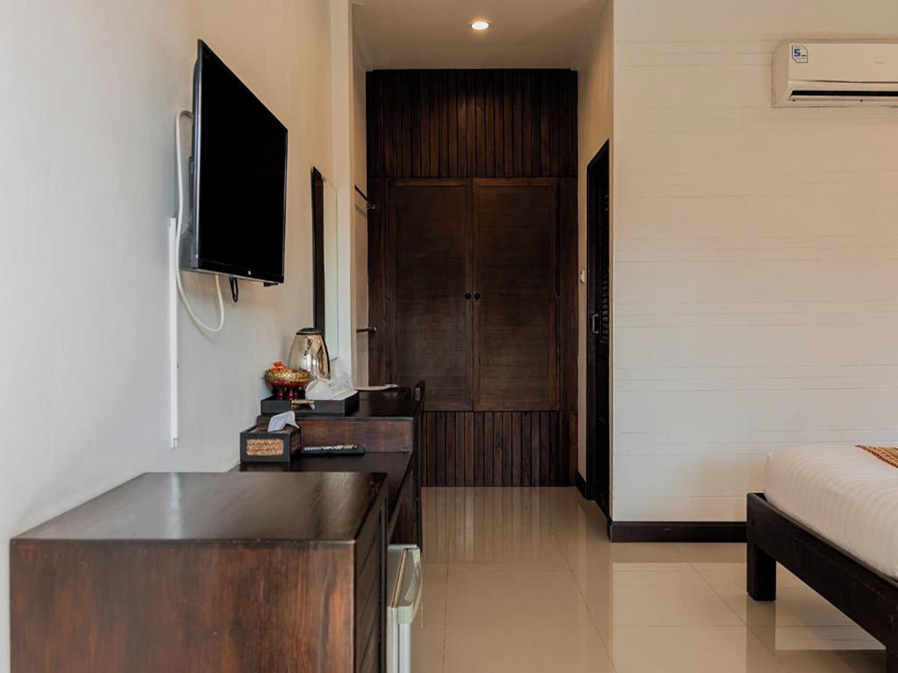 A hotel room with a wooden desk, a flat-screen TV, a wardrobe, and a bed.