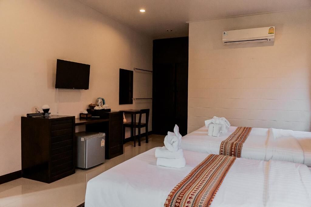 A hotel room with two beds, a desk, a television, and an air conditioning unit.