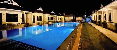Vista nocturna de un área de piscina con habitaciones de hotel cercanas.