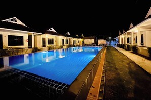Vista nocturna de un área de piscina con habitaciones de hotel cercanas.
