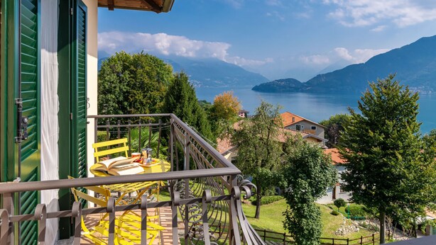 En balkon med et gult bord og stole, der ud til et sølandskab og bjerge.