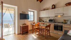 Et hyggeligt køkken med trægulv, et spiseområde med bord og stole, et fjernsyn ophængt på væggen og en balkon med udsigt.