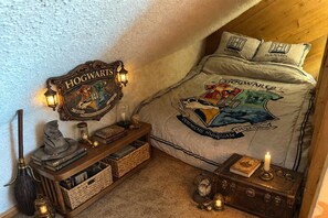 Une chambre avec une couvre-lit aux couleurs de Poudlard, un panneau décoratif fixé au mur, et une petite table sur laquelle sont posés des livres et un globe terrestre.
