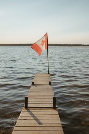 Un muelle de madera que se extiende hacia aguas tranquilas, con una bandera canadiense al final.