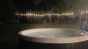 A hot tub in a backyard with string lights and red chairs.