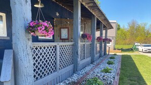 A porch with a wooden railing, hanging flower baskets, and a gravel pathway leading to the house.