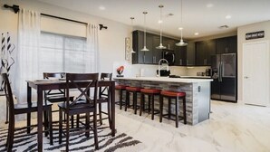 Une cuisine moderne avec des meubles de couleur sombre, un plan de travail en marbre et un îlot central doté de tabourets de bar.