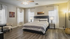Une chambre à coucher avec un lit, des tables de chevet, un ventilateur de plafond et une fenêtre avec des rideaux.