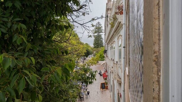 A narrow cobblestone street lined with trees and buildings, with outdoor seating and a few people visible. - Setúbal Prime IV, Apartment (Setúbal)